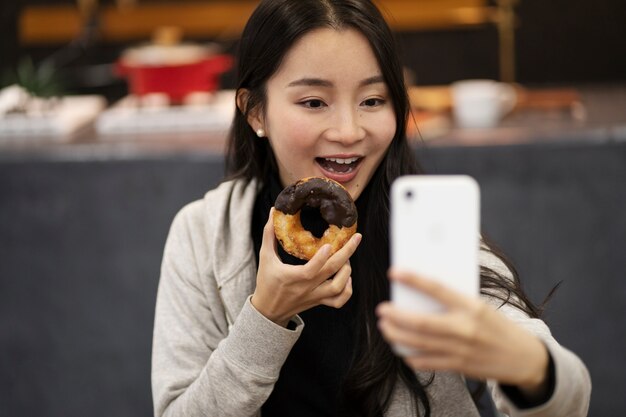 Japanese woman taking selfie while eating a doughnut