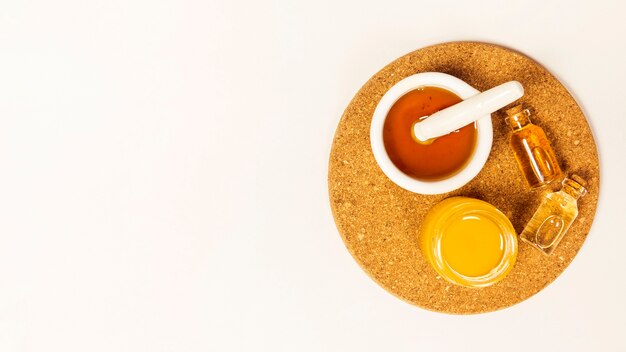 Jar of honey and essential oil on brown cork over white background