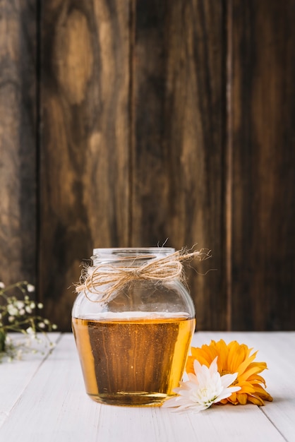 Jar of honey with beautiful flowers on wooden surface