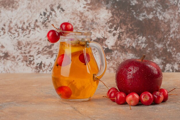 A jar of juice decorated with cherries and apple on marble table.