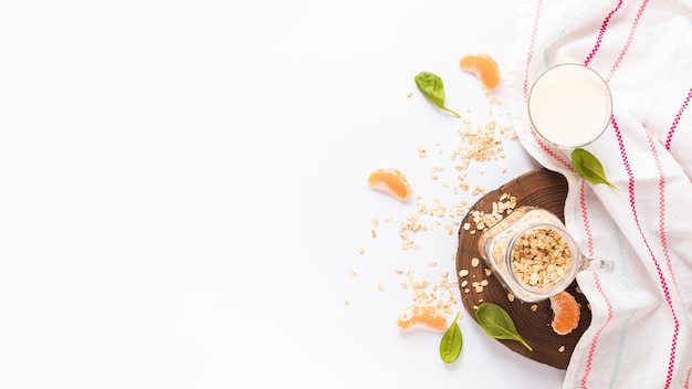 Jar of oats; basil leaves; orange slices; milk and napkin over white background