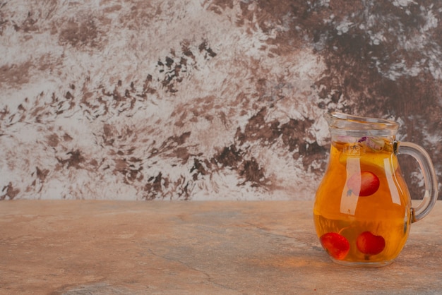 A jar of peach juice with cherries on marble table.