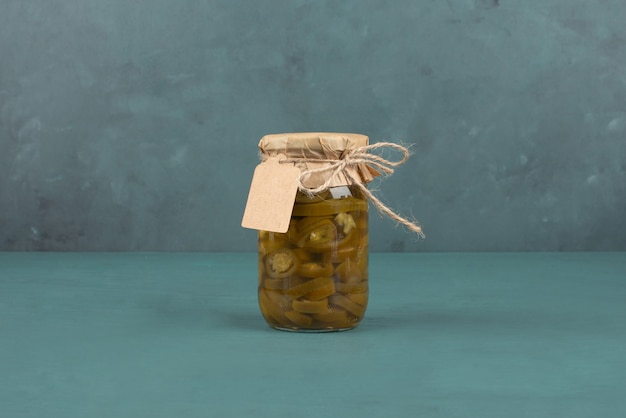 Jar of pickled green jalapenos and picture frame on blue table. 