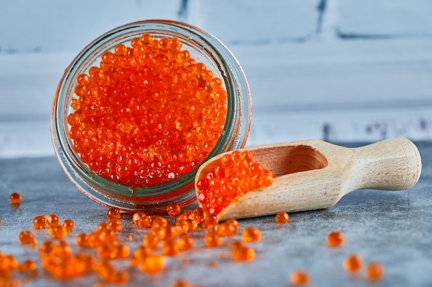 A jar of red caviar and wooden spoon on marble background.