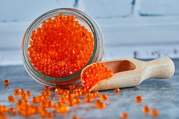Free photo a jar of red caviar and wooden spoon on marble background.