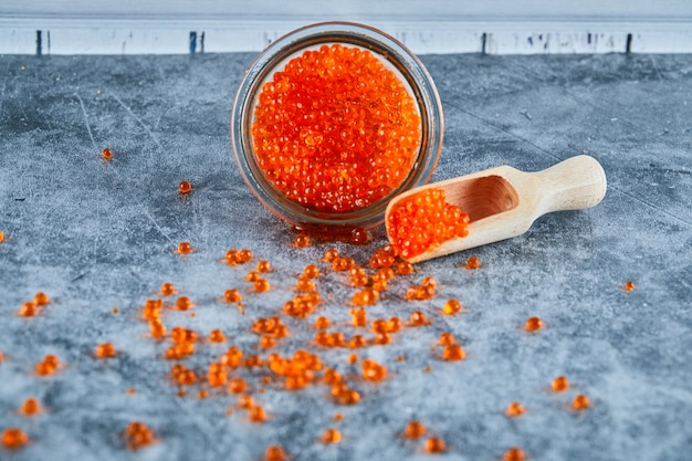 Foto gratuita un barattolo di caviale rosso e cucchiaio di legno su sfondo marmo.