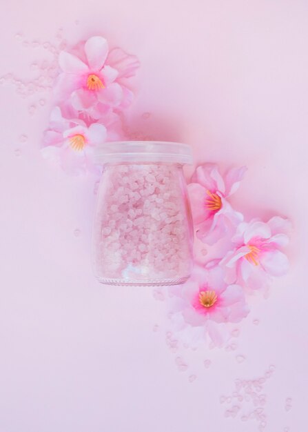 Jar of salt and artificial flowers on pink backdrop