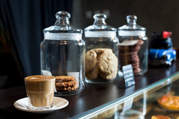 カフェのカウンターでラテコーヒーカップと様々なクッキーの瓶