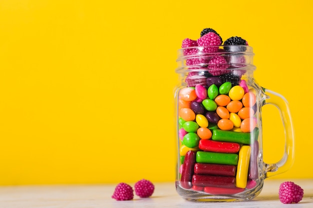 Jar with candies on bright yellow background