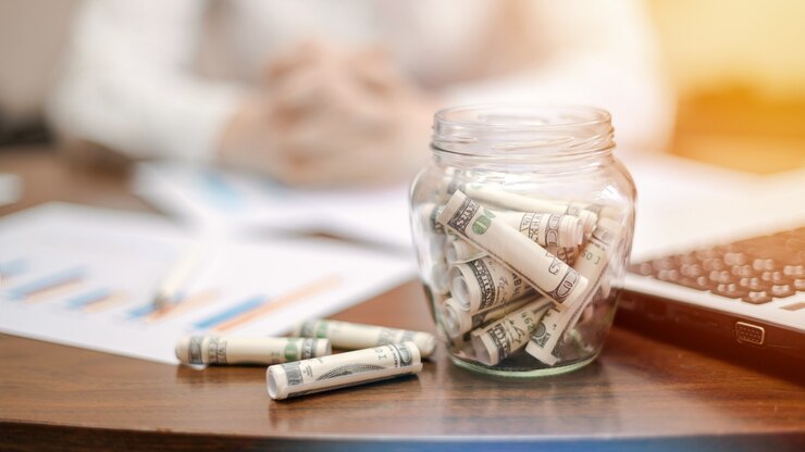 Free Photo a jar with rolled banknotes on the table. laptop, papers, woman on the background