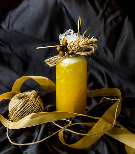 A jar of yellow cocktail decorated with dry herbs and threads on the top.