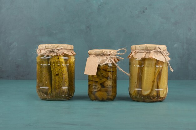 Jars of pickled cucumbers and jalapenos on blue table.