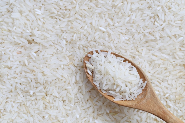 Рис жасмина в деревянной ложке на предпосылке белого риса.