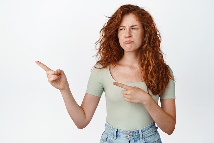 मुफ़्त फोटो jealous teen redhead girl pointing looking left with upset moody face standing disappointed against white background