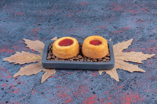 Желейные торты и кофейные зерна в небольшом подносе на абстрактном столе.