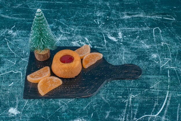 Jelly filled cake, marmelades and a tree figurine on a black board on blue background. High quality photo