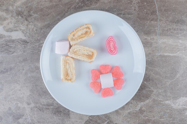 jelly sweets, marshmallows and cake roll slices on a platter on marble surface