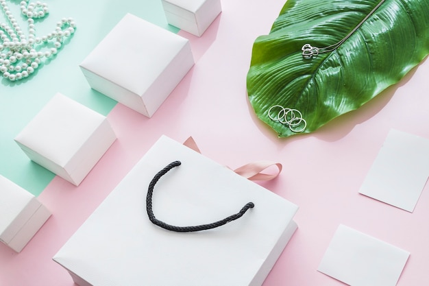 Free photo jewelry with white boxes and leaf on paper backdrop