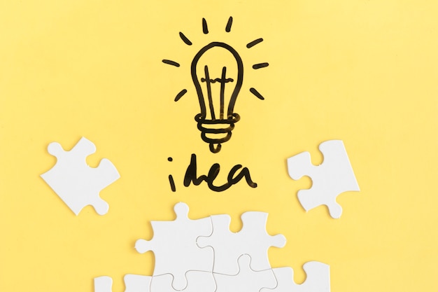 Jigsaw puzzle and light bulb with idea word on yellow background