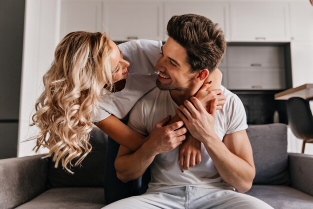 Jocund curly woman embracing husband with love. Brunette man looking at girlfriend with smile.