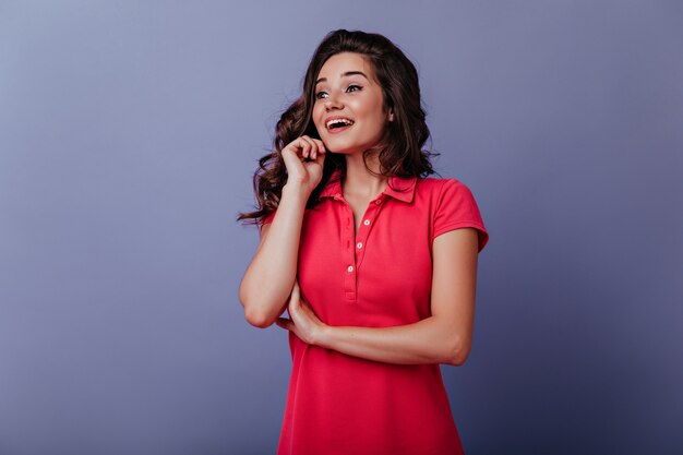 Jocund graceful woman looking away with inspired smile. Curly dark-haired girl expressing amazement.