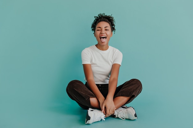 Jocund woman posing with tongue out on turquoise wall