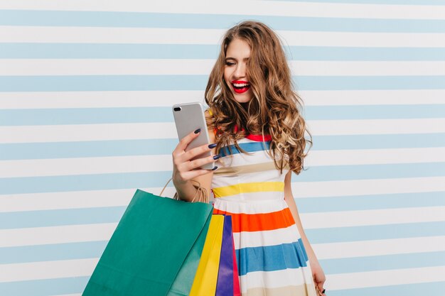 Jocund woman with light-brown wavy hair making selfie after shopping. Pretty smiling girl funny posing on striped wall.