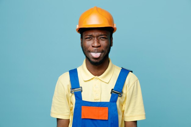 Jokin showing tongue young african american builder in uniform isolated on blue background