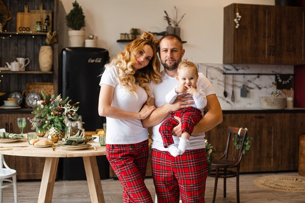 Jolly Caucasian family in family look wearing white t-shirt and red trousers. Father holding baby.