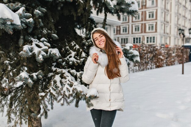 Joy, happiness of amazing beautiful girl smiling in warm winter clothes on fri tree full with snow space.