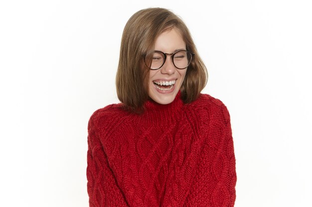Joy and happiness concept. Pretty girl in stylish eyewear and warm cozy sweater having fun indoors, enjoying funny story or joke, being in good mood. Attractive young female laughing out loud