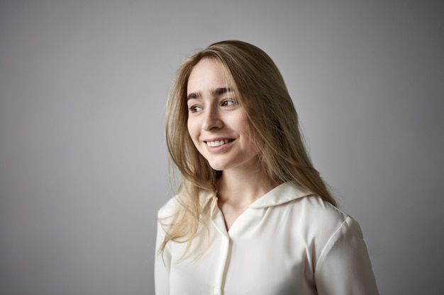 Concetto di gioia, felicità e sentimenti positivi. ritratto di giovane donna dai capelli biondi amichevole in elegante camicia bianca che sorride felicemente, rallegrandosi di buone notizie, presente, esami o successo sul lavoro