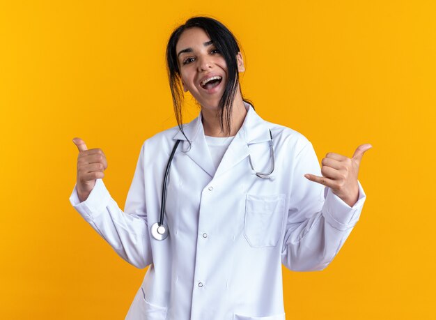 Joydul looking at camera young female doctor wearing medical robe with stethoscope showing different gesture isolated on yellow wall