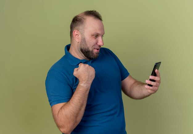 Радостный взрослый славянский мужчина держит и смотрит на мобильный телефон, делая жест да