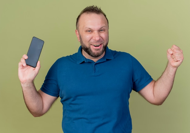 Joyful adult slavic man holding mobile phone doing yes gesture 