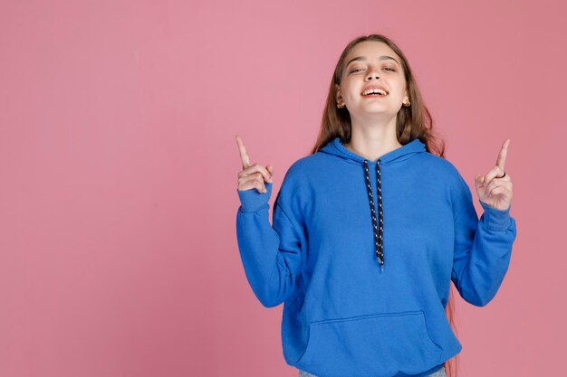 Joyful attractive lady having fun while pointing up with both index fingers isolated on pink