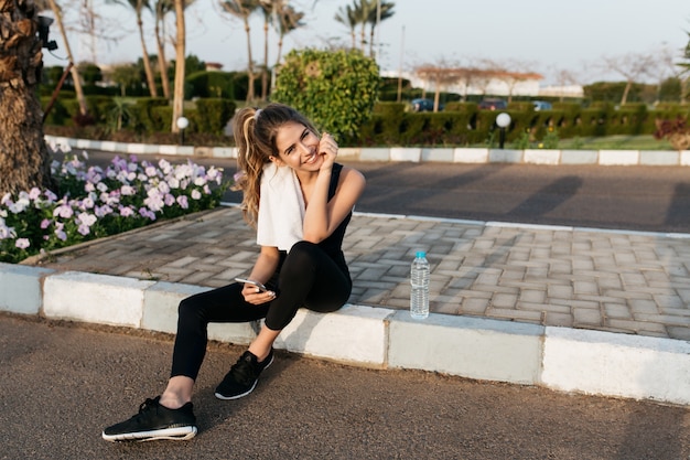 晴れた朝に外でリラックスできるスポーツウェアでうれしそうな魅力的な若い女性。笑顔、熱帯都市、夏の時間、トレーニング、フィットネス、トレーニング。