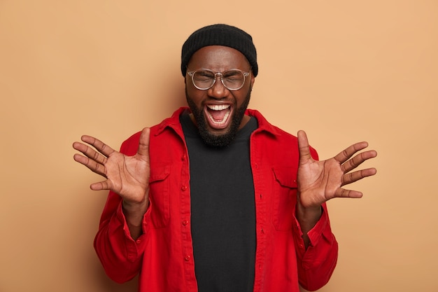 Joyful bearded guy spreads palms, keeps mouth opened, laughs out from positive emotions