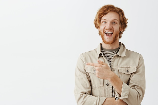 Joyful bearded redhead guy posing against the white wall