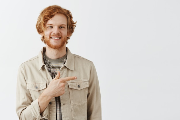 Joyful bearded redhead guy posing against the white wall