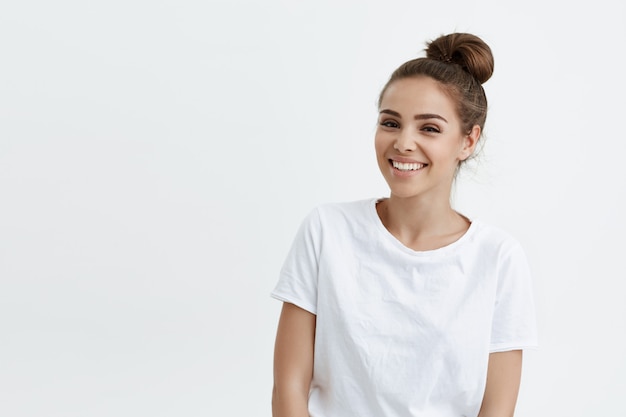 Joyful beautiful caucasian woman with bun hairstyle wearing t-shirt, expressing cheer and good mood