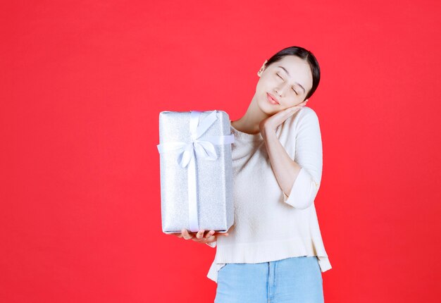 Joyful beautiful woman holding gift box and stand on red wall