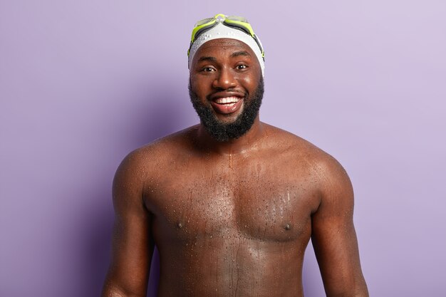 Joyful black man has strong body, shows wet torso, enjoys recreation time and swimming