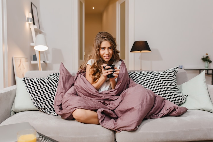 Free Photo joyful brown-haired young woman posing with interested face expression, while sitting under blanket