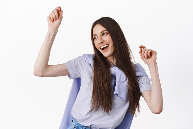 Joyful brunette girl dancing and having fun, enjoying leisure, looking happy aside at logo, standing over white background