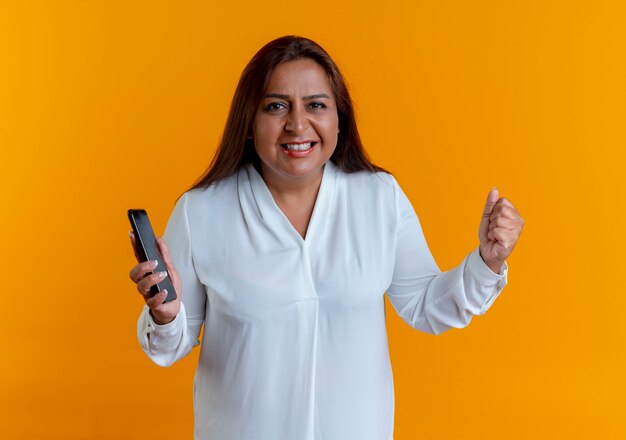 Joyful casual caucasian middle-aged woman holding phone and showing yes gesture 