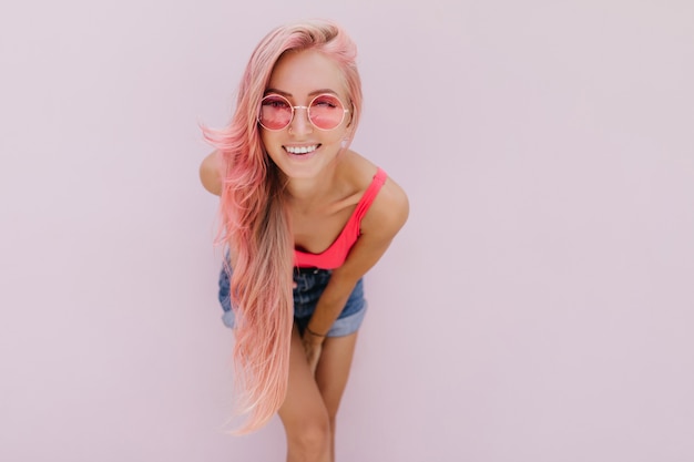 귀여운 미소로 포즈를 취하는 분홍색 머리를 가진 즐거운 백인 여자.