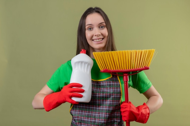 Joyful cleaning young woman wearing uniform in red gloves holding mop with cleaning agent on isolated green wall