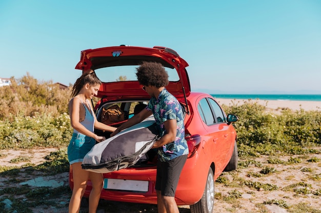 Joyful couple getting things out of trunk on beach