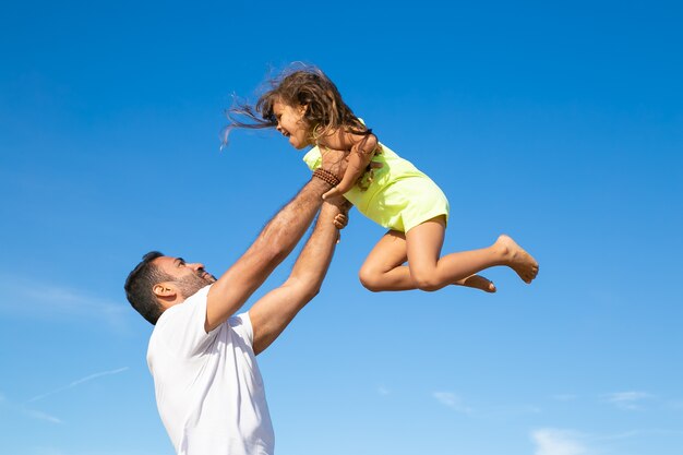 Joyful dad holding excited girl and throwing hands up in air